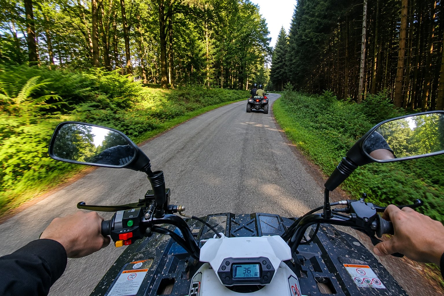 Vue conducteur en quad sur une route en forêt avec un quad devant